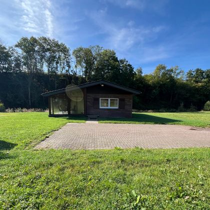 Une maison en bois confortable entourée d'herbe verte et d'arbres. Le ciel est clair et bleu.
