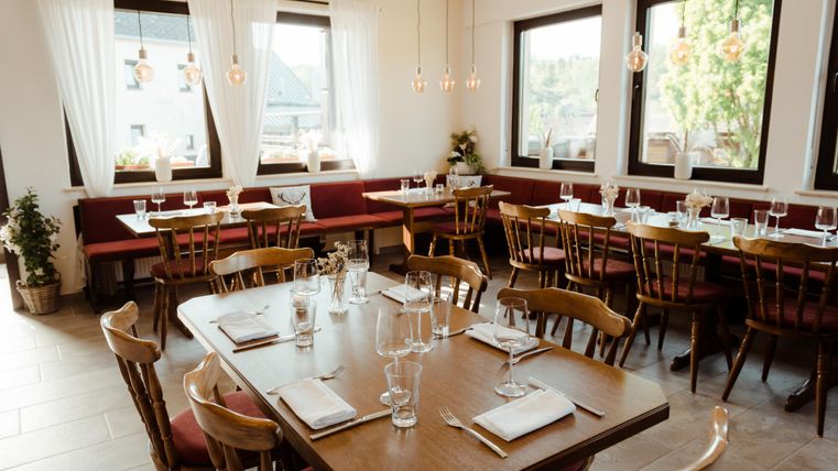Ein einladendes Restaurant mit Holztischen und Stühlen. Große Fenster sorgen für viel Tageslicht und eine gemütliche Atmosphäre.