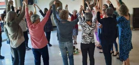 Eine Gruppe von Frauen steht im Kreis und hält sich die Hände. Alle haben die Arme hochgehoben und scheinen Freude zu haben.