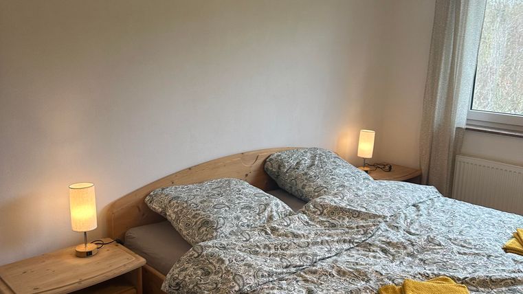 Ein gemütliches Schlafzimmer mit einem Doppelbett und zwei Nachttischen. Die Bettwäsche ist gemustert und es liegen gelbe Handtücher auf dem Bett.