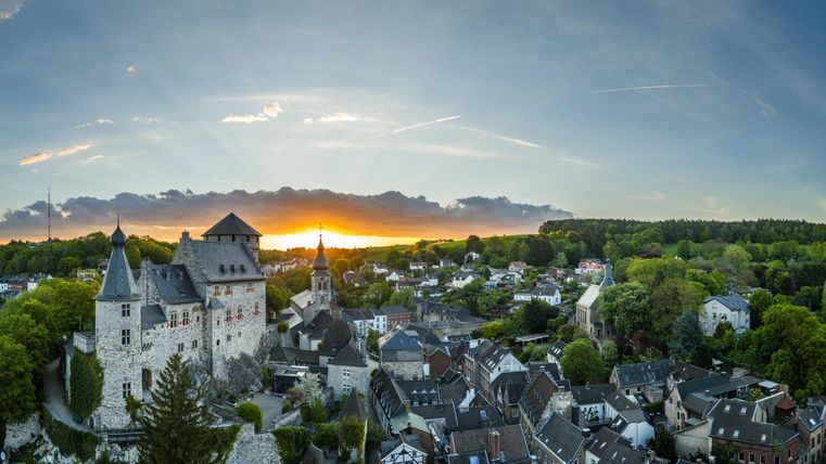 An impressive view of a castle at sunset. The surrounding landscape is green and the buildings of the town are clearly visible.