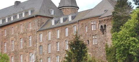 Ein historisches Gebäude mit grauem Dach und Steinfassade. Umgeben von grünen Bäumen und einer malerischen Landschaft.