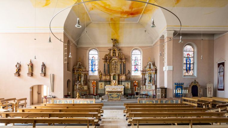 Een mooie kerk met een hoge toren staat te midden van groene bomen en huizen. De heldere blauwe lucht complementeert het idyllische tafereel.