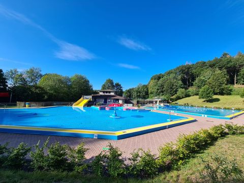 A beautiful outdoor swimming area with a blue swimming pool and a slide facility. Surrounded by trees and a green meadow, the place radiates peace and relaxation.