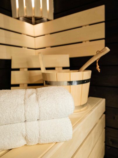 Ein gemütlicher Saunabereich mit hellen Holzlatten. Darin liegen zwei saubere Handtücher und ein Eimer mit einem Holzlöffel.