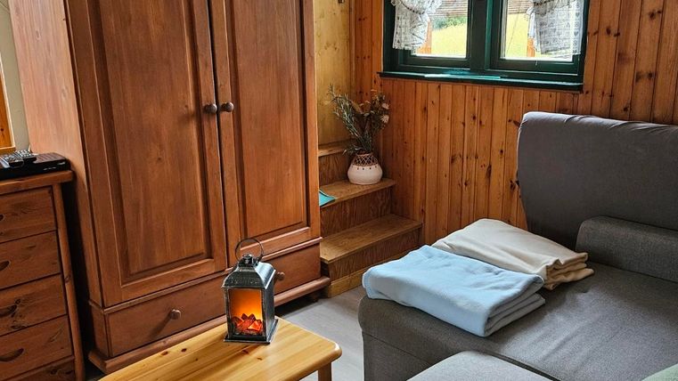 A cozy living space with a gray sofa and a wooden cabinet. On the table, there is a lantern and next to it are blankets.