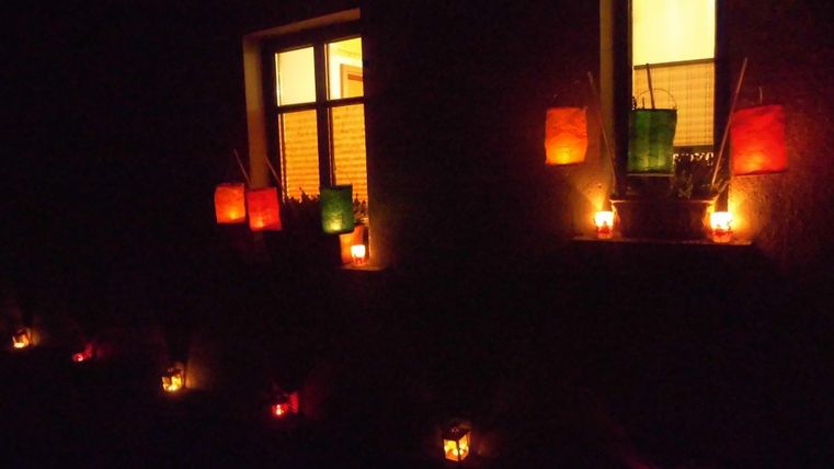 A atmospheric facade with illuminated windows and colorful lanterns. In the dark, the lights radiate a cozy atmosphere.