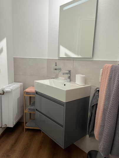 Une salle de bain moderne avec un lavabo élégant et un grand miroir.
L'aménagement est lumineux et fonctionnel, avec un sol en bois et des teintes douces.