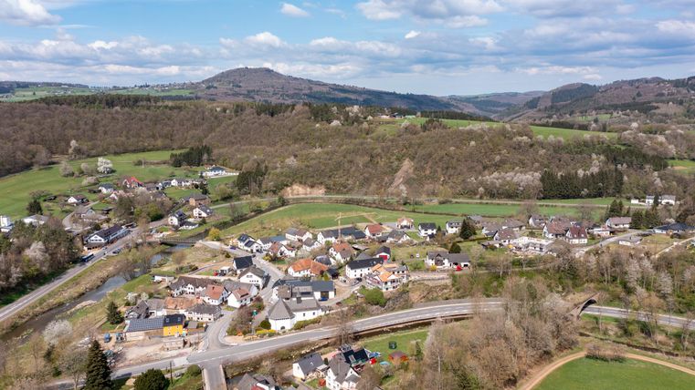 Een schilderachtig landschap met een klein dorp omgeven door heuvels en bossen. De huizen zijn mooi gegroepeerd en een straat loopt door de scène.