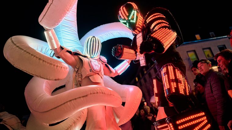 Une performance créative avec des costumes éclatants et une figure impressionnante. La scène se déroule la nuit et attire l'attention des spectateurs.