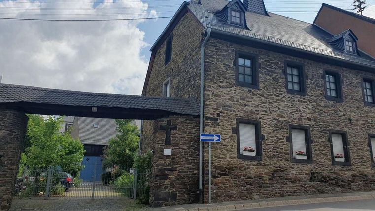 Un bâtiment historique en pierre avec un belvédère marquant. Au premier plan, on peut voir des arbres et une zone d'entrée.