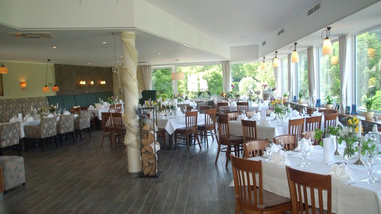 An elegant restaurant with set tables and a large window overlooking a beautiful garden. The decor is modern and inviting.