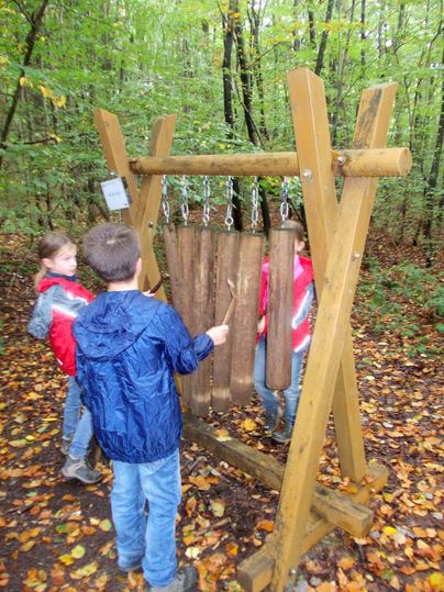 Des enfants jouent à une station sonore en bois dans la forêt.