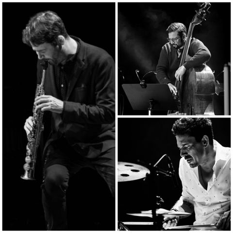 Drei Musiker, die leidenschaftlich auf der Bühne spielen. Ein Saxophonist, ein Kontrabassist und ein Schlagzeuger, festgehalten in einem stimmungsvollen Schwarz-Weiß-Bild.