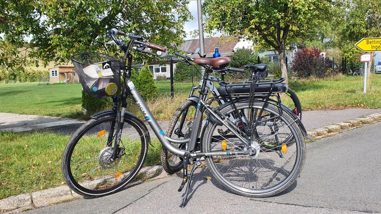 Zwei Fahrräder stehen an einer Straße in Ingendorf, neben einem Wegweiser nach Bettingen.