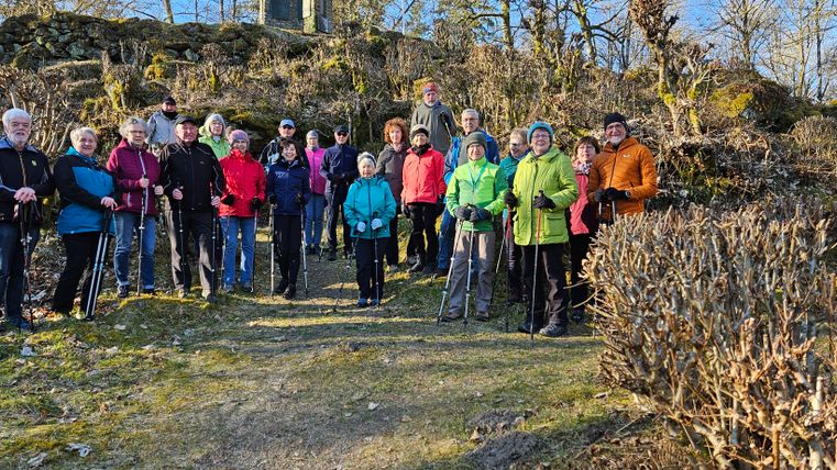 Eine Gruppe von Läufern joggt entlang eines Sees. Im Hintergrund sind grüne Wiesen und ein Dorf mit einer Kirche zu sehen.