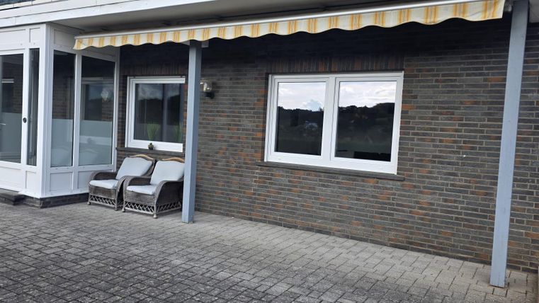 A terrace with two chairs and a stone privacy screen. Above the terrace there is a sunshade.