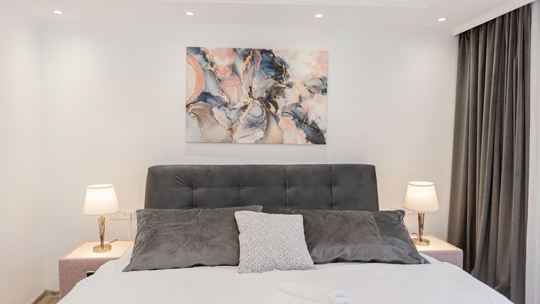 An elegant bedroom with a gray bed and soft pillows. A modern artwork hangs on the wall, and two bedside lamps create a cozy atmosphere.