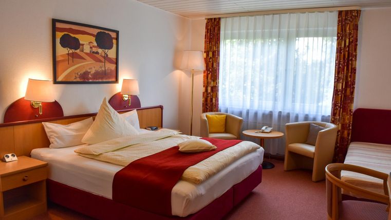 A cozy hotel room with a large bed and comfortable armchairs. The room is bright and inviting, with a window that lets in natural light.