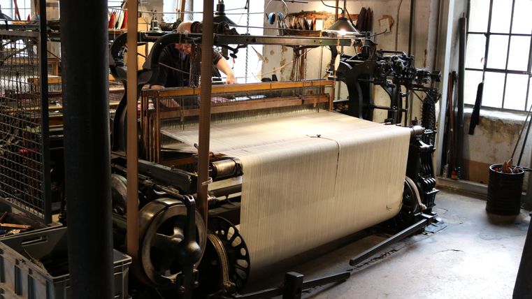 Weefgetouw in het LVR Industriemuseum-Tuchfabrik Müller met werkend persoon.