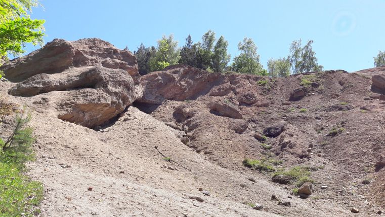 A rocky landscape with steep slopes and scattered trees. The sky is clear and blue.