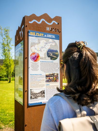 A person stands in front of an information sign outdoors. The sign explains the flood in the Ahr Valley and displays maps and images.