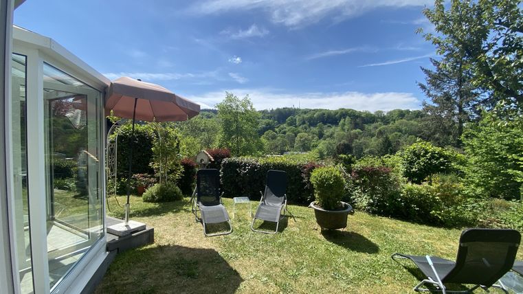 A beautiful garden with deck chairs and a sunshade. In the background, hills and trees are visible under a clear blue sky.