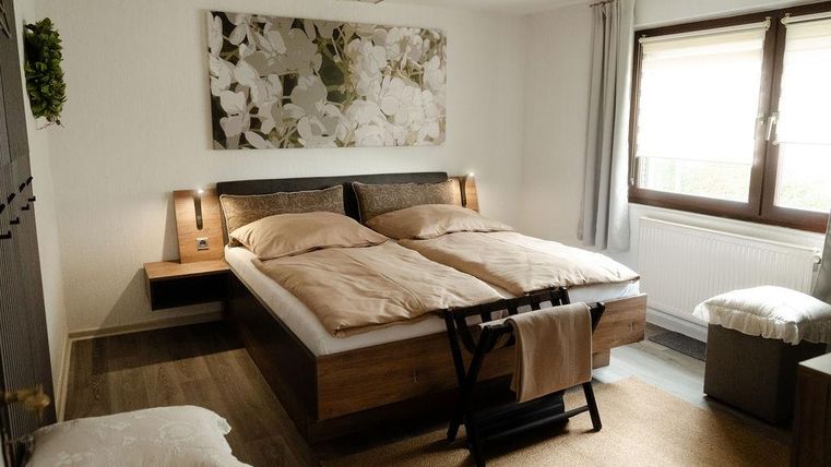 Une chambre moderne avec un lit double et des couettes claires. Les murs sont discrètement décorés, et de grandes fenêtres permettent une lumière naturelle.