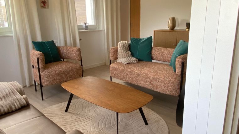 Un salon moderne avec deux fauteuils élégants et un canapé. La table en bois est posée sur un tapis rond et les murs sont peints en clair.