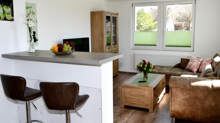 A bright and modern living kitchen with a cozy sofa and a coffee table. In the background, you can see large windows that let in plenty of daylight.