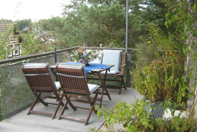 Ein gemütlicher Balkon mit Holzstühlen und einem Tisch. Umgeben von Pflanzen und einem ruhigen Ausblick.