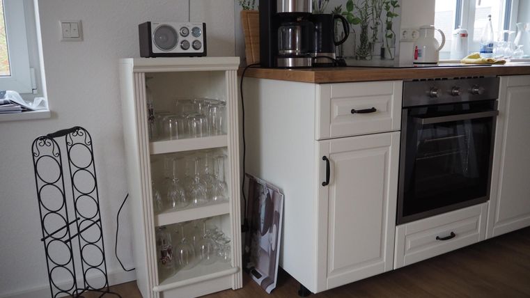 Eine moderne Küche mit einem Holzarbeitsbereich und Küchengeräten. Im Vordergrund steht ein Regal mit Gläsern und ein stilvoller Weinständer.