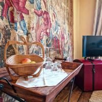 A rustic wooden board with a basket full of apples and glasses stands in front of a tapestry. In the background, a television is visible.