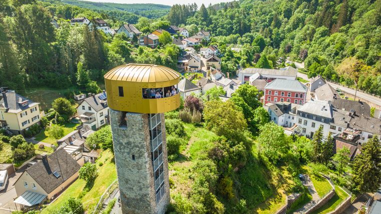 Luchtfoto van een toren met een gouden uitkijkplatform in een groen landschap met huizen.