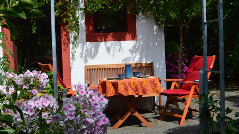 Ein einladender Gartenbereich mit einem Tisch und Stühlen. Bunte Blumen umgeben die Sitzecke und schaffen eine gemütliche Atmosphäre.