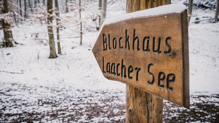 Un panneau indicateur dans la forêt enneigée. Il montre la direction vers le chalet au lac de Laacher.
