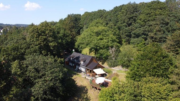 A charming house surrounded by lush greenery and trees. The clear sky and sunny atmosphere create an inviting environment.