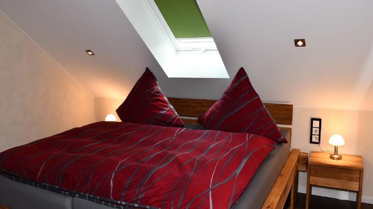 A cozy bedroom with a large double bed and red pillows. The room has a skylight and a bedside lamp.