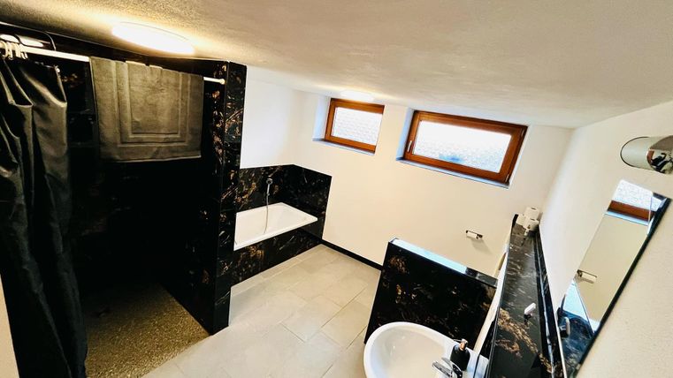 Een modern badkamer met een douche en een badkuip. Heldere muren en ramen zorgen voor een aangename lichtsfeer.