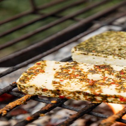 Gegrillter Käse mit Kräutern und Gewürzen auf einem Rost. Der Käse ist goldbraun und befindet sich über offenen Flammen.