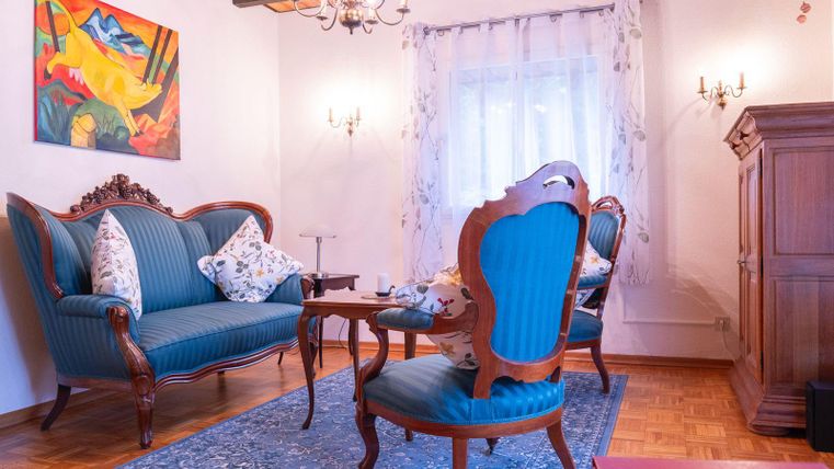 Un salon confortable avec un canapé bleu et un fauteuil élégant. Les murs sont décorés d'art et d'un rideau, et un tapis apporte de la chaleur à la pièce.