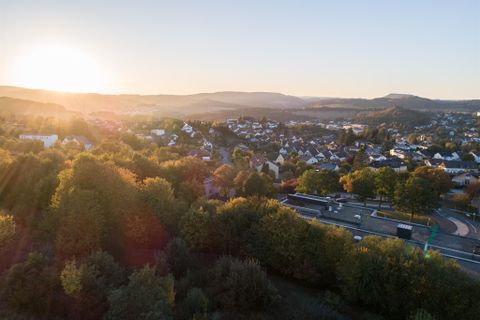 Ein malerischer Ausblick auf eine Stadt im Sonnenaufgang. Umgeben von Bäumen und sanften Hügeln.