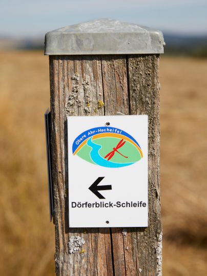 Een houten paal met een wandelbord wijst naar de Dörferblick rondwandeling in de OberAhr-Hocheifel.