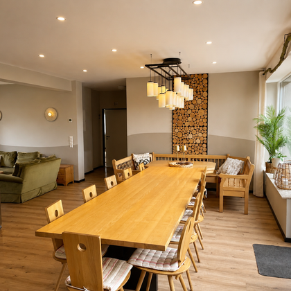 Een moderne keuken met een lange houten tafel en comfortabele houten stoelen. De ruimte is helder verlicht en heeft grote ramen met uitzicht op een groene omgeving.