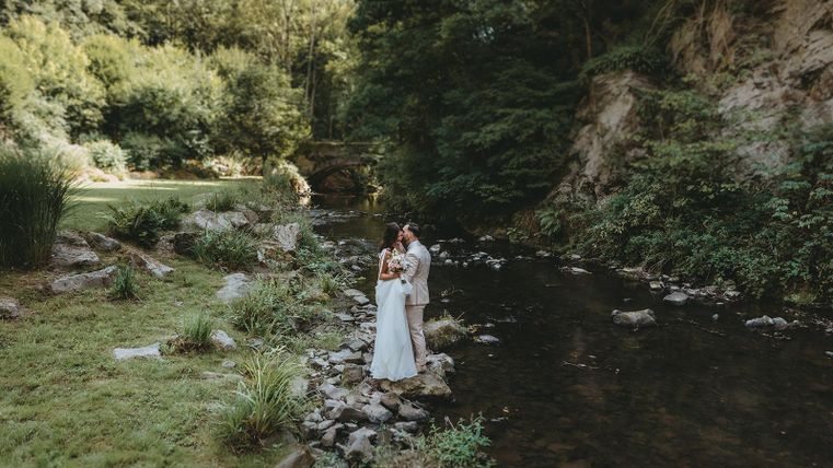 Un couple romantique se tient au bord d'un petit ruisseau clair, entouré d'une verdure luxuriante. La scène est paisible et idyllique, idéale pour un instant spécial.