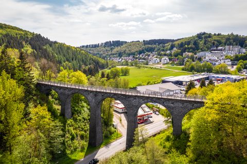 Luftaufnahme des Daun Viadukts auf dem Maare-Mosel-Radweg, umgeben von grünen Wäldern und einer Stadt im Hintergrund.