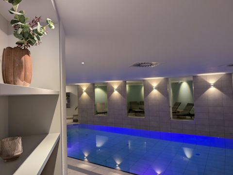 Une piscine intérieure avec de l'eau bleue dans une salle de spa éclairée chaleureusement.