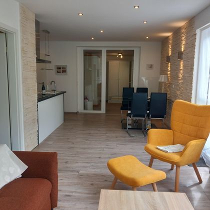 Een moderne woonkamer met een oranje stoel en een rode bank. Op de achtergrond staat een eettafel met blauwe stoelen.