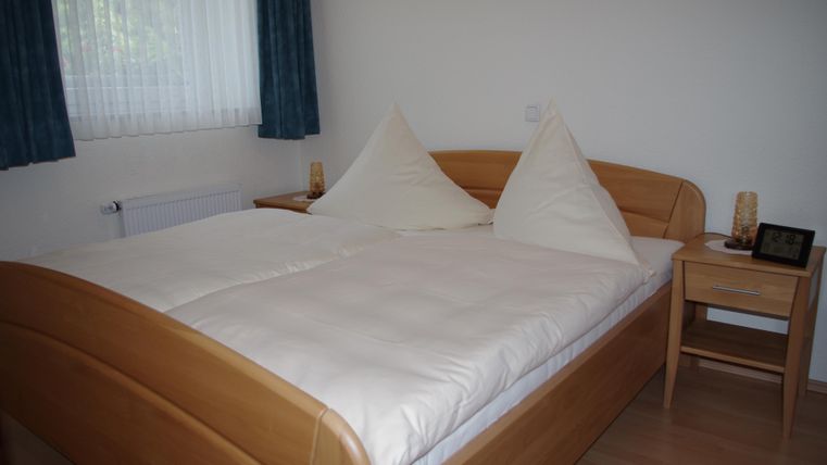 Ein gemütliches Schlafzimmer mit einem Doppelbett aus Holz und schönem Bettzeug. Neben dem Bett steht ein Nachttisch mit einer Lampe und einem kleinen Bildschirmschoner.