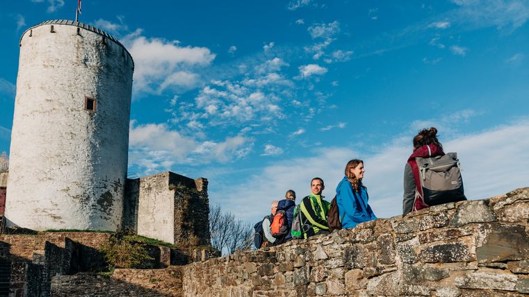 Des personnes assises sur un mur près du château de Reifferscheid, ciel bleu.